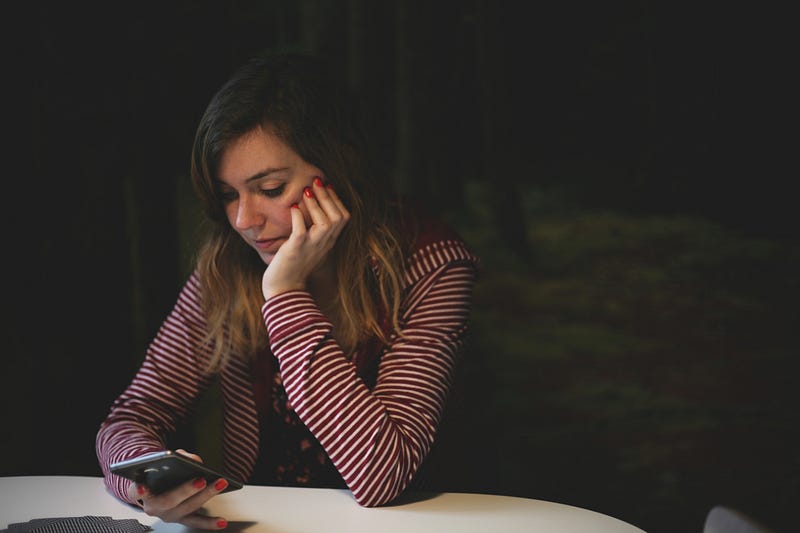 A woman sitting at a table staring at her phone.