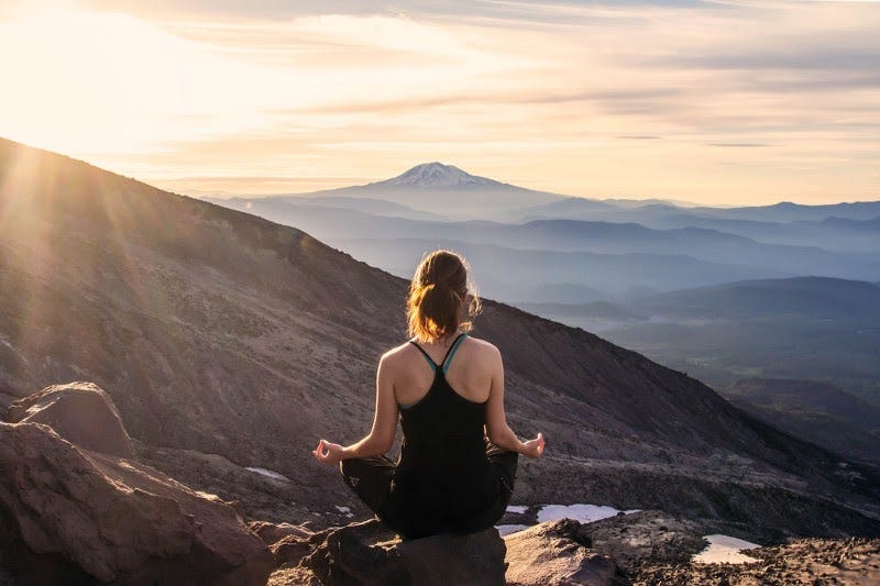 A woman meditating on a rocky mountain looking out over a beautiful view.
