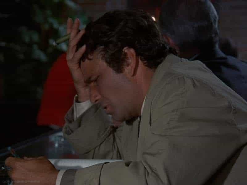 Columbo sits at a bar, forehead in palm, thinking very hard about something.