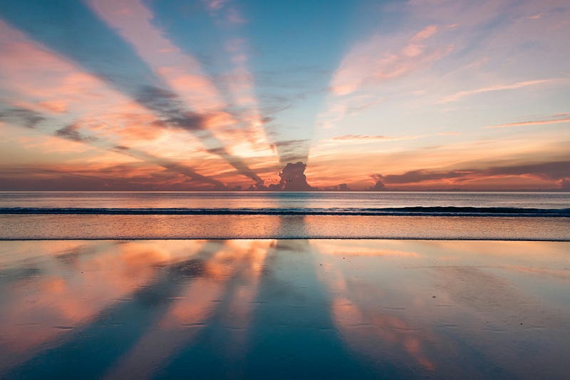 A beuatiful image of the sun setting in the distance, behind a large body of water.