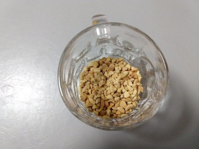 Top view of a drinking glass containing a small amount of crushed peanuts.