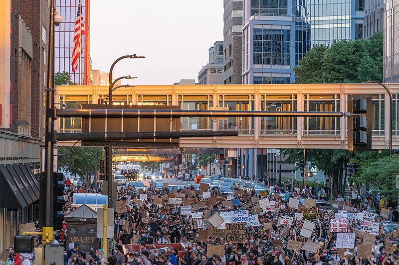 Downtown Minneapolis swarmed by a large group of Black Lives Matter Protesters marching down a street while holding signs.