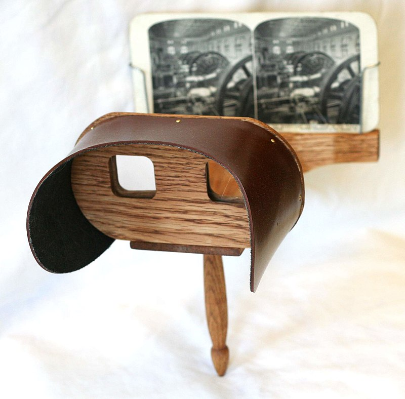 A wooden stereoscope with eyeholes to look through points at a book with two similar images in parallax.