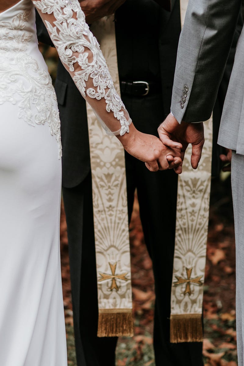 A picture of a couple getting married by a priest.