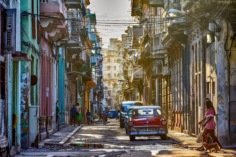 looking down a Cuban city street, old cars and power lines strung across haphazardly