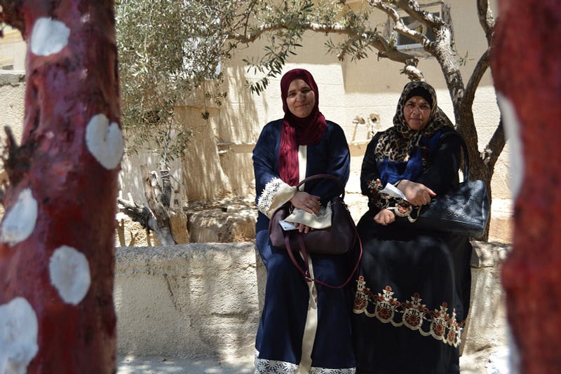 Two Syrian refugee women sit under a tree.