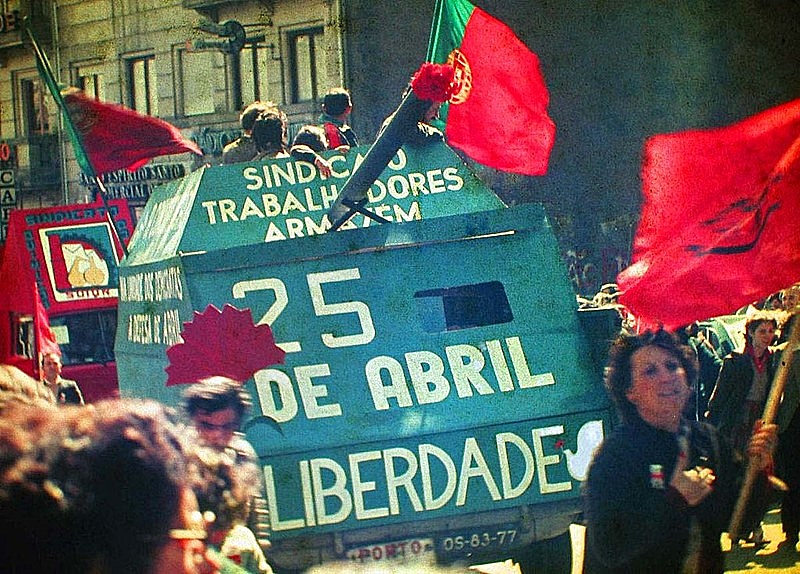 Tanque marcha com os dizeres “25 de abril, liberdade”. A multidão de Porto carrega bandeiras portuguesas e cravos vermelhos — inclusive no canhão.Tanque marcha com os dizeres “25 de abril, liberdade”. A multidão de Porto carrega bandeiras portuguesas e cravos vermelhos — inclusive no canhão.