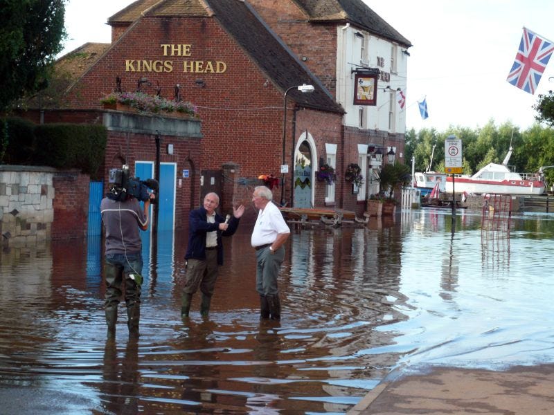 Two men standing in flood water outside a pub.