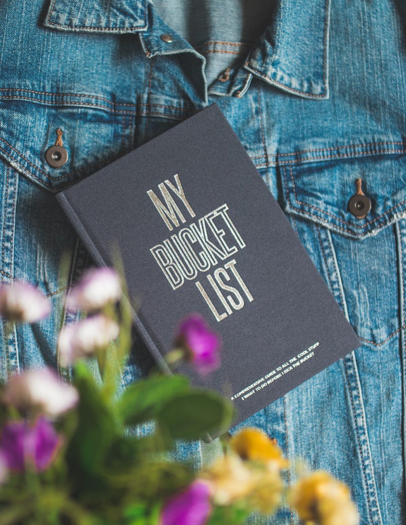 A few flowers and a diary that read “My Bucket List” placed on a denim jacket.