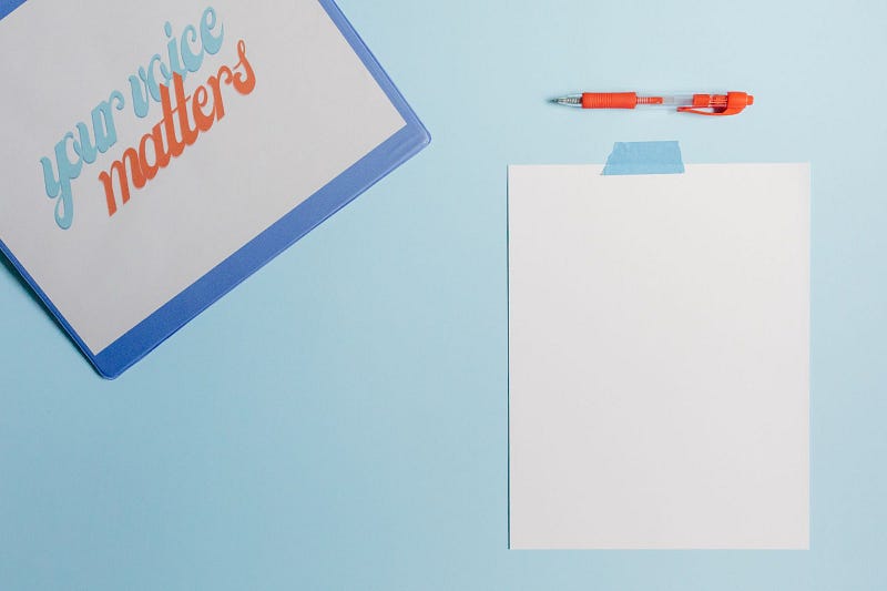 a paper with the words "your voice matters" written on it, an orange clicker pen, and a blank piece of paper, all placed on top of a blue desk