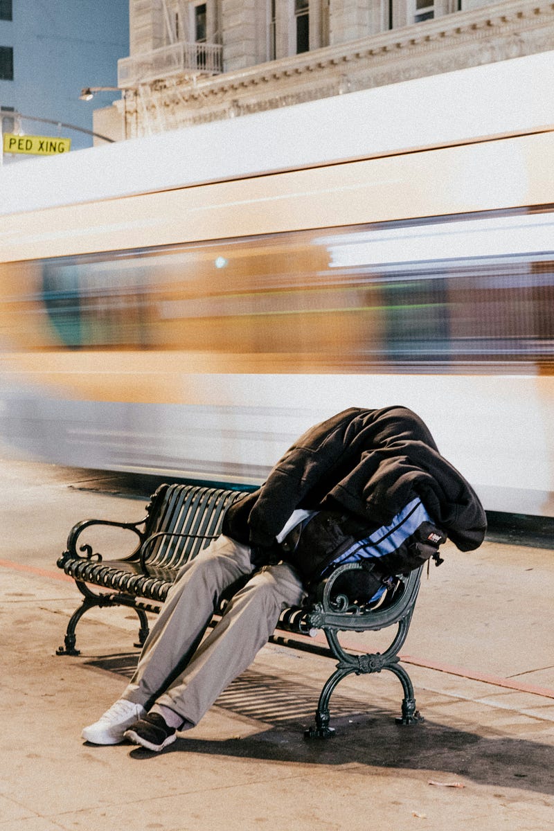 A person on a bench sleeps under a jacket.