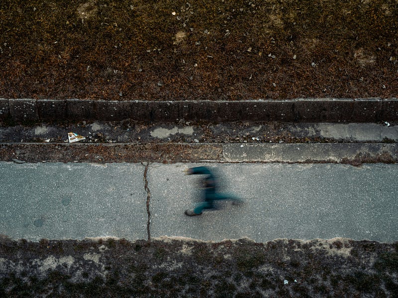 A blurry image of a person walking on a sidewalk. The photos is take with a bird’s eye view.