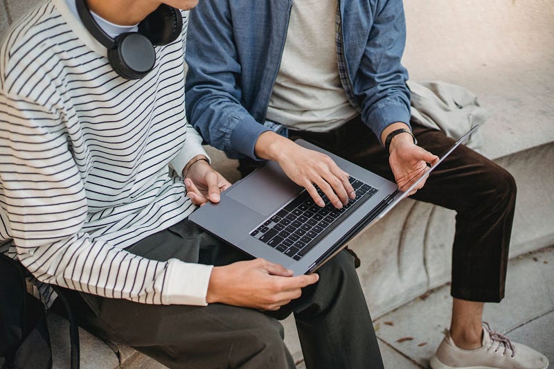 two people sitting beside each other while holding a laptop