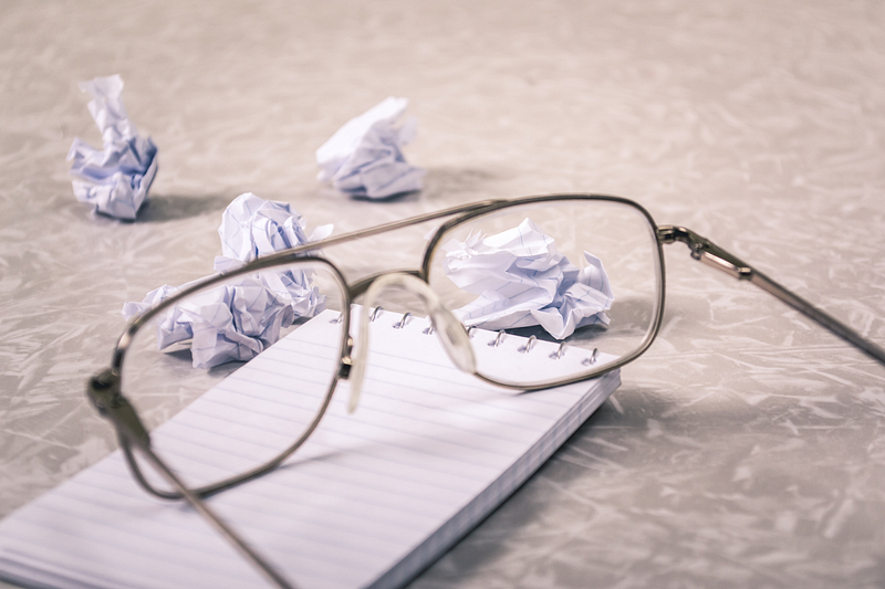 eyeglasses on top of a notepad beside crumpled pieces of paper