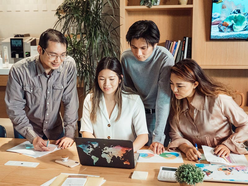 four people gathered while looking at a single laptop