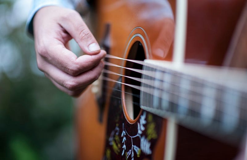 A photo of pale white photos strumming a guitar decorated with painted flowers.