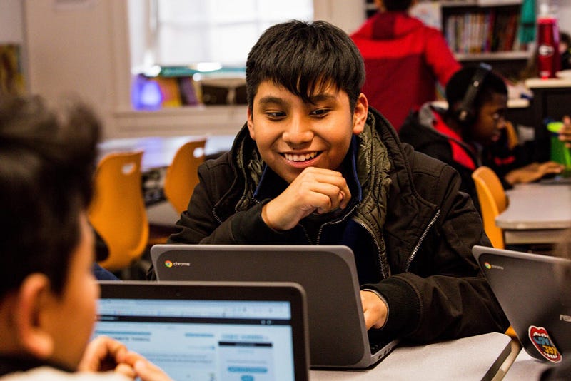 A student smiles looking at his laptop. 