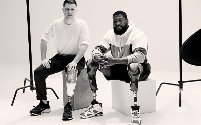 Image of two men sitting together for a photo session, each one has a prosthetic limb that looks futuristic.