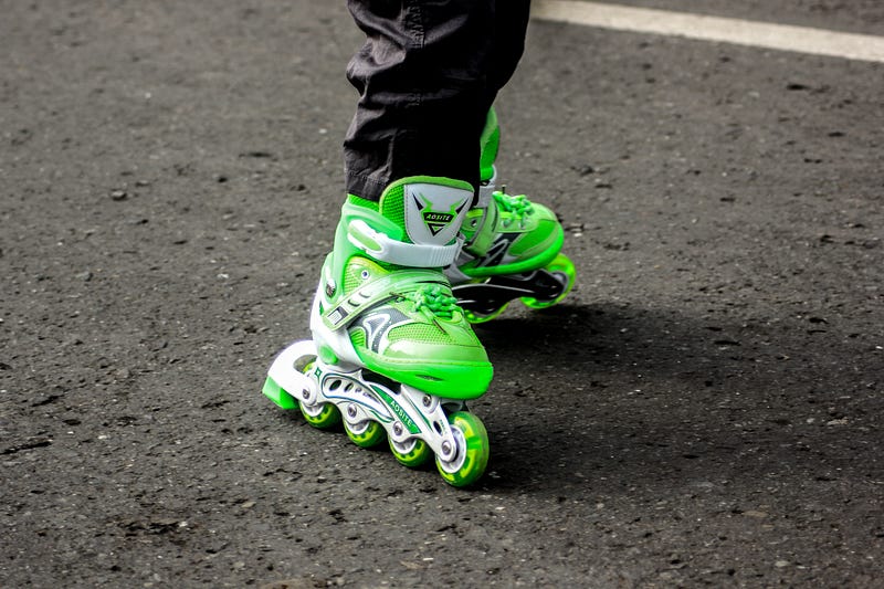 A man rolling down the street in green rollerblades