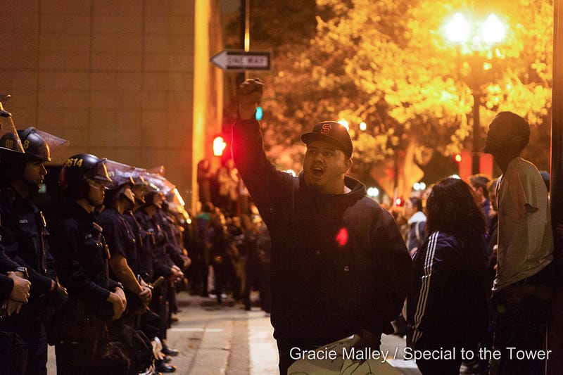 As the protest continues late into the evening on July 7, Oakland police officers keep watch while a demonstrator chants in protest against police brutality.