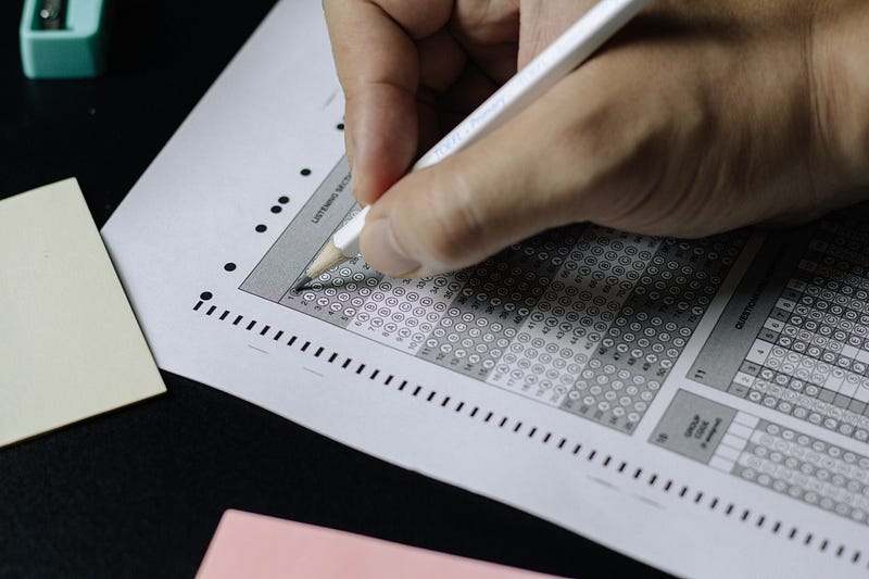 A persons hand filling in an exam sheet with a pencil