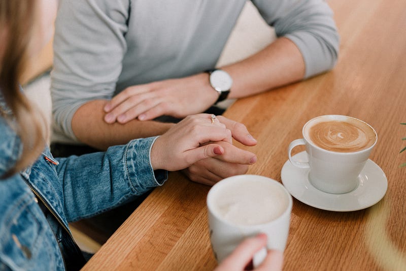 A man and woman are having coffee. The woman has a wedding ring on and is holding the man’s hand.