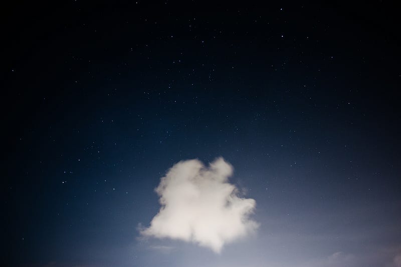A lone fluffy cloud against a dark sky speckled with stars