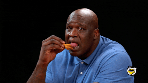 Shaq licking a wing and making a face to indicate that the sauce is hotter than he expected