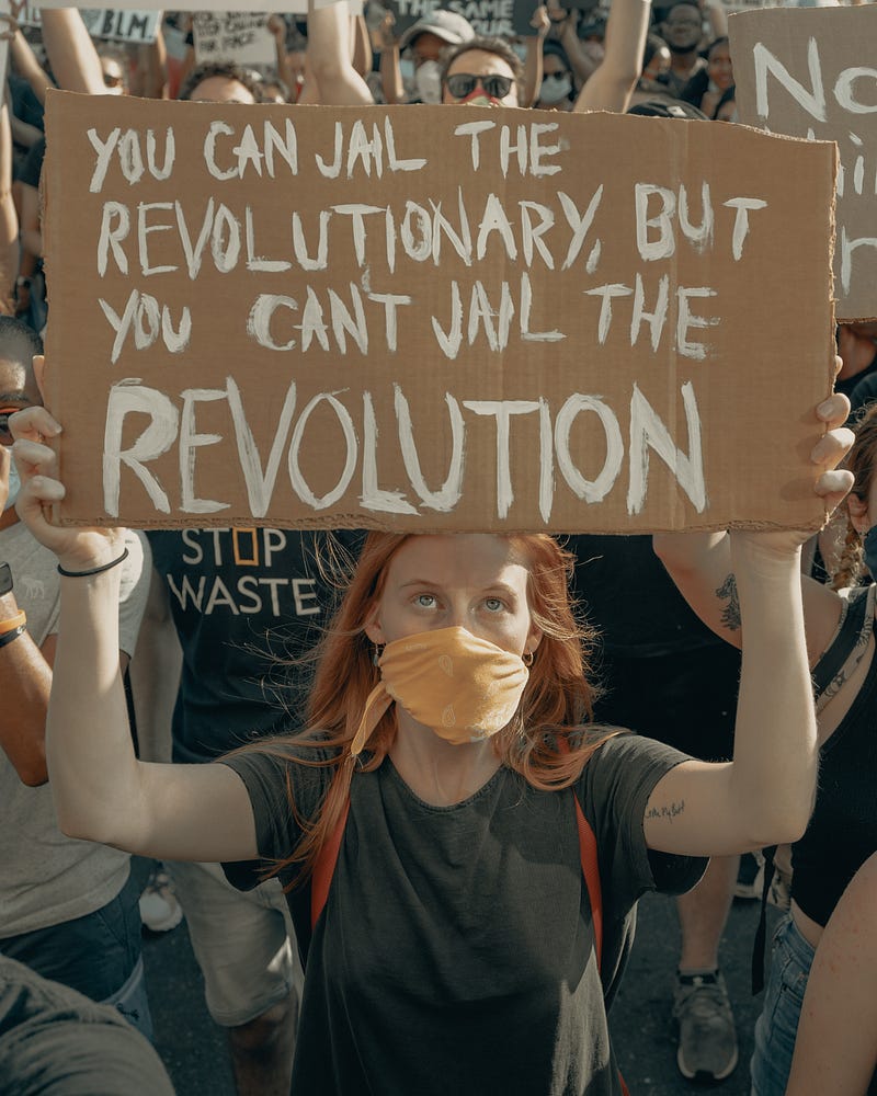 A protestor holding a sign, “ You can jail the revolutionary but you can’t jail the revolution”