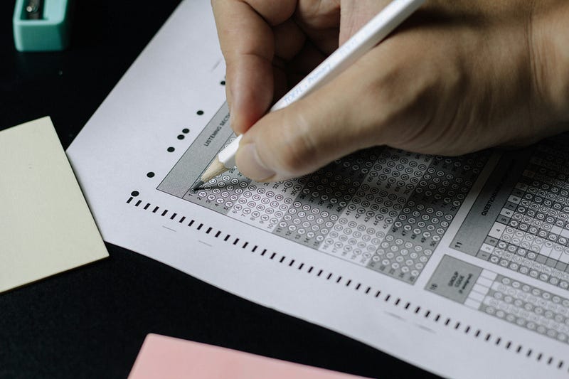 A hand filling in bubbles on a scantron test sheet.