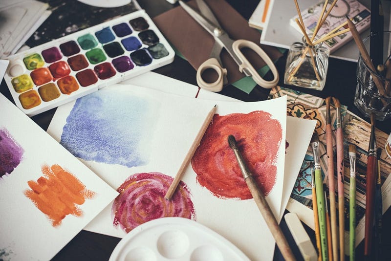 Mess in the the artist's studio, watercolor paints, brushes and sketches, palette and painting tools. Designer's working place, hipster style.