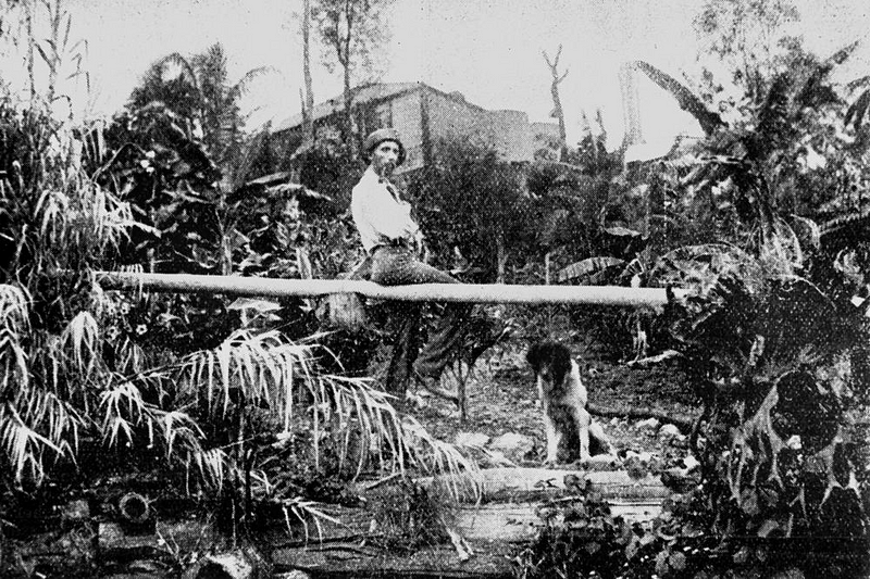 A man sits smoking a pipe on a felled tree.