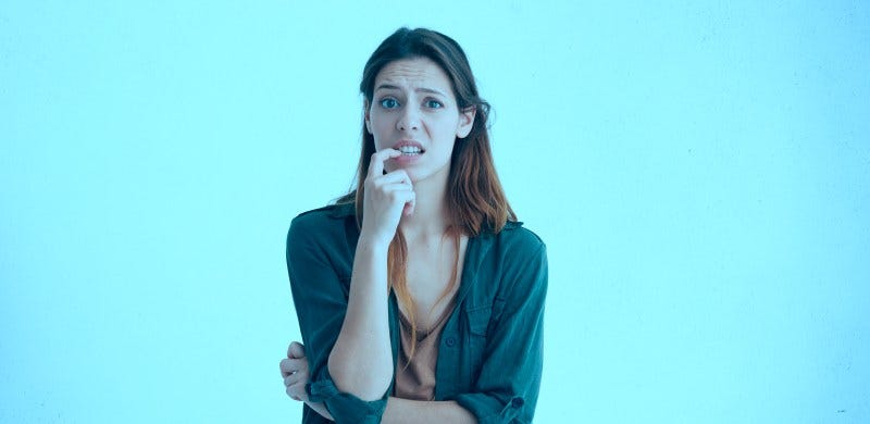 Imagem de uma mulher de cabelos escuros e pele clara, expressando dúvida, com um dos dedos na boca, como se estivesse mordendo a unha.