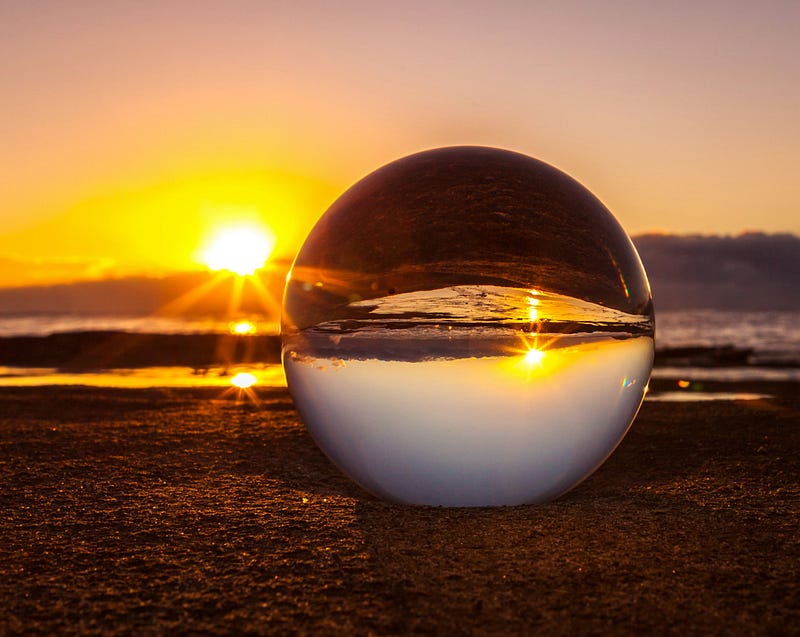 The sun sets in the background, with a foreground glass ball inverting the scene.