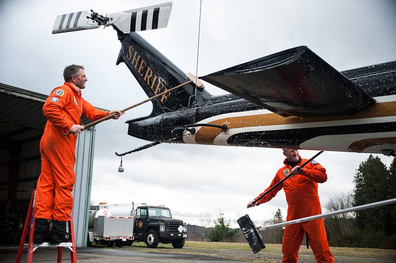 Ernie Zeller (left) and Oyvind Henningsen (right) help to clean SnoHawk 10 following a rescue training exercise in the mountains. Upon landing and securing the main rotor blades the entire five-man crew sets to work on their post-flight duties of cleaning and checking all aspects of the UH-1H helicopter. 