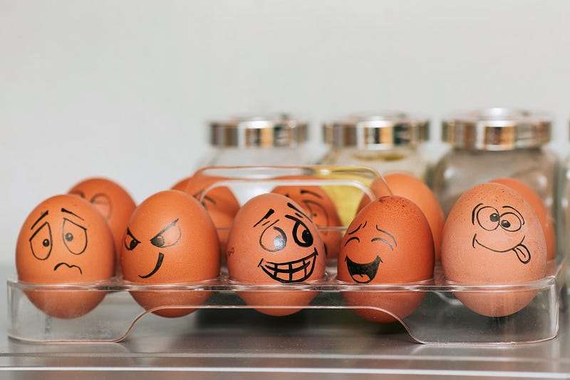 A dozen brown eggs in the refrigerator with drawn on faces of various emotions