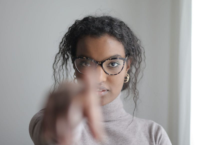 a person with glasses and curly hair pointing at the camera