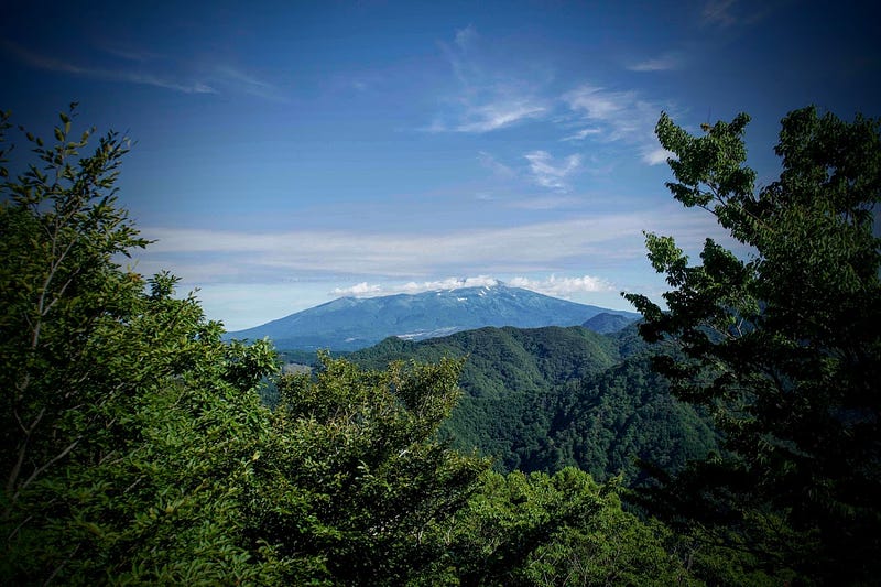 The summit of Mt. Chokai shrouded in cloud in the distance underneath a deep blue sky. Image taken from the summit of Mt. Kyogakura, one of the 100 Famous Mountains of Yamagata in Sakata City, in the Tohoku region of North Japan