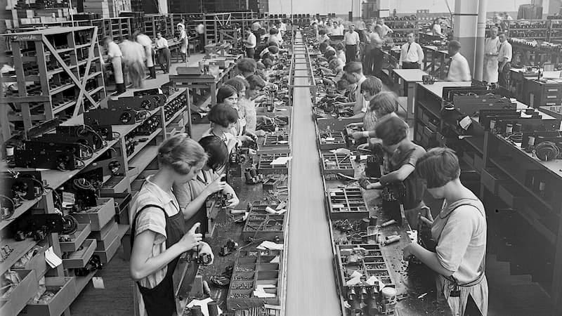 Uma foto em preto e branco de mulheres trabalhando em uma linha de montagem.