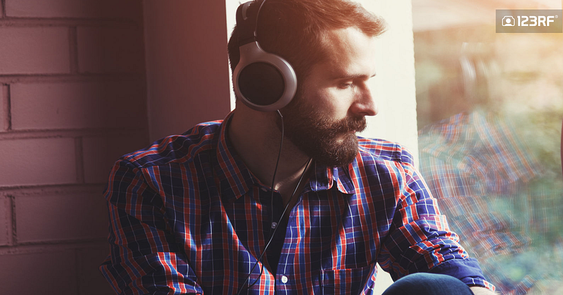 Stock Photo - stylish bearded man in headphones listening to music near window with reflection