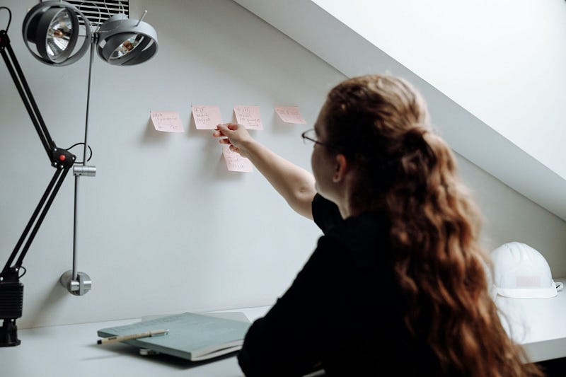 a person applying the eat the frog principle while sticking pink notes on the wall