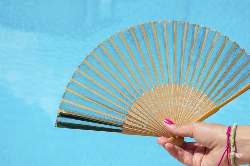Fan in girls hand with clear blue water in background. Save from the summer heat