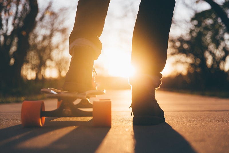 The silhouette of a person riding a skateboard with orange wheels at sunset at University of Northern Iowa