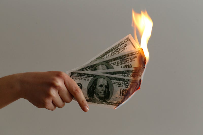 A person’s hand holding four burning $100 bills