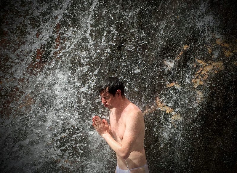 Tim Bunting AKA The Kiwi Yamabushi (mountain monk) stands beneath a raging waterfall during waterfall meditation on Mt. Yudono