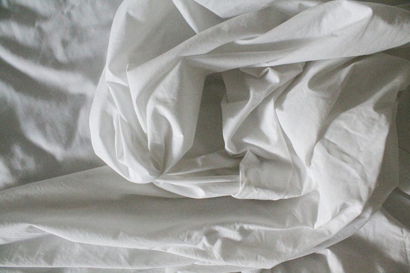 White sheets curled up in closeup on a mattress.