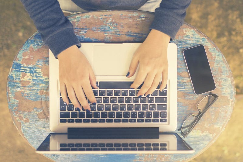 Girl sits at a table with a laptop and cell phone