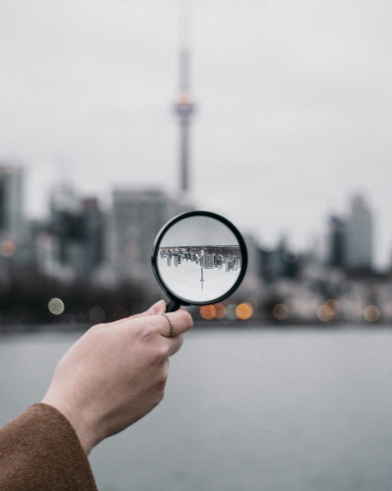 A person holds a magnifying glass, inverting how we see a distant skyline.