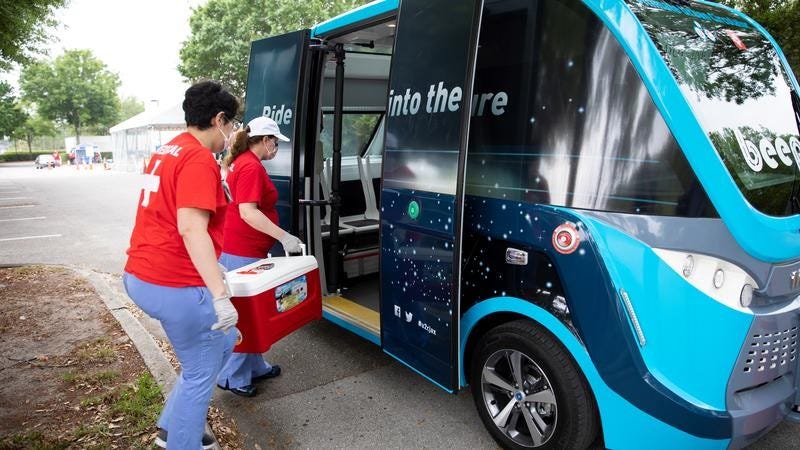 Medical workers load testing samples into a Navya autonomous vehicle