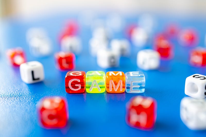 dice with letters on a table. in the middle of the table are four dice arranged to spell the word game.